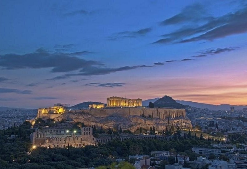The Acropolis floodlit at dusk, seen from a hill across the city