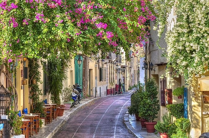 A lane in Plaka under bougainvillea, café tables along the pavement